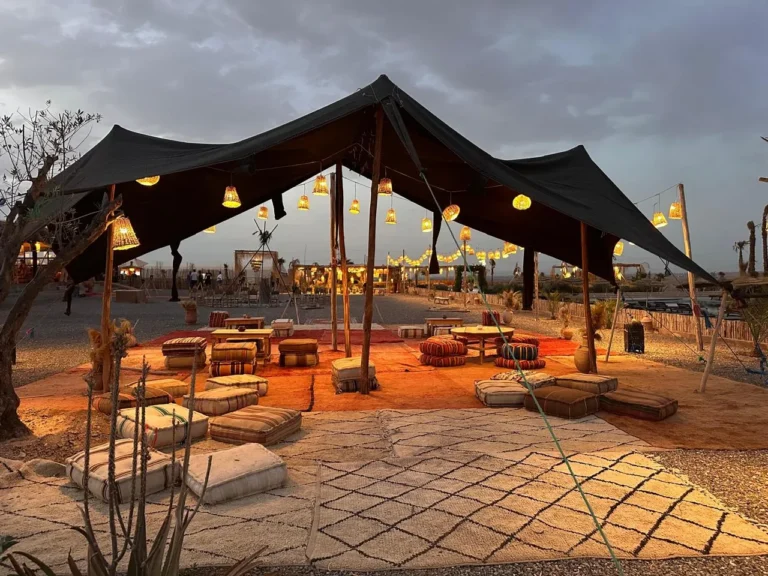 Open tent with lanterns and floor cushions at an Agafay desert camp at dusk