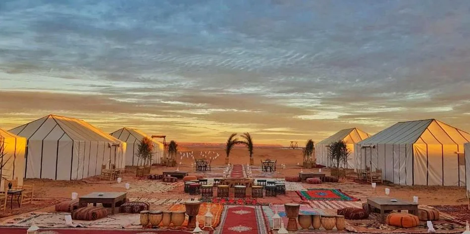 White tents and a lounge area with rugs at a desert camp at sunset