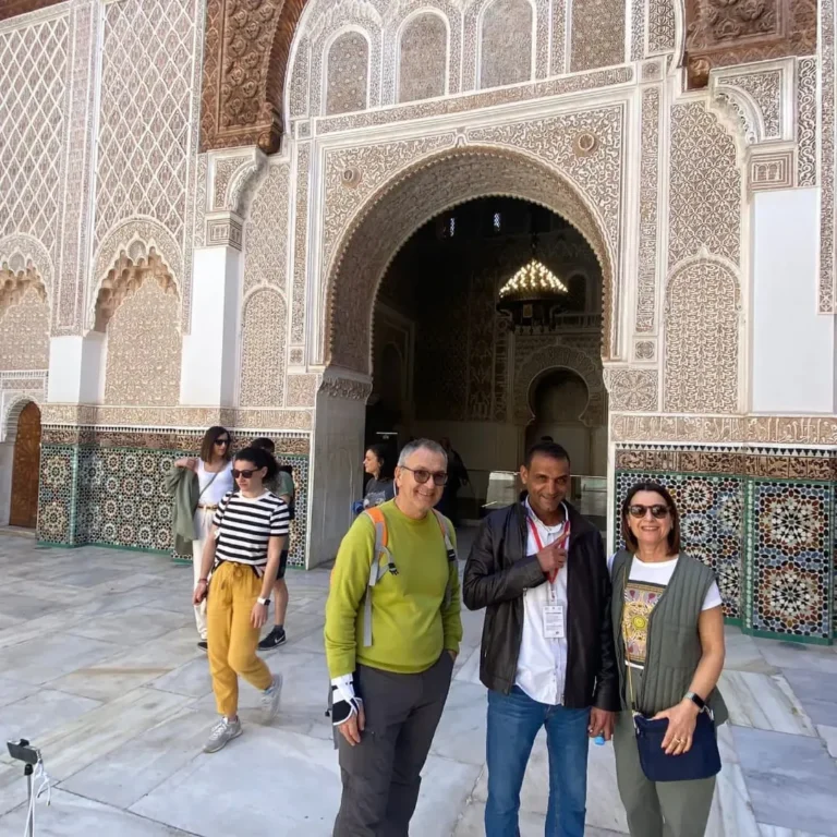 Visitors below the carved stucco arch of a madrasa courtyard in Marrakech