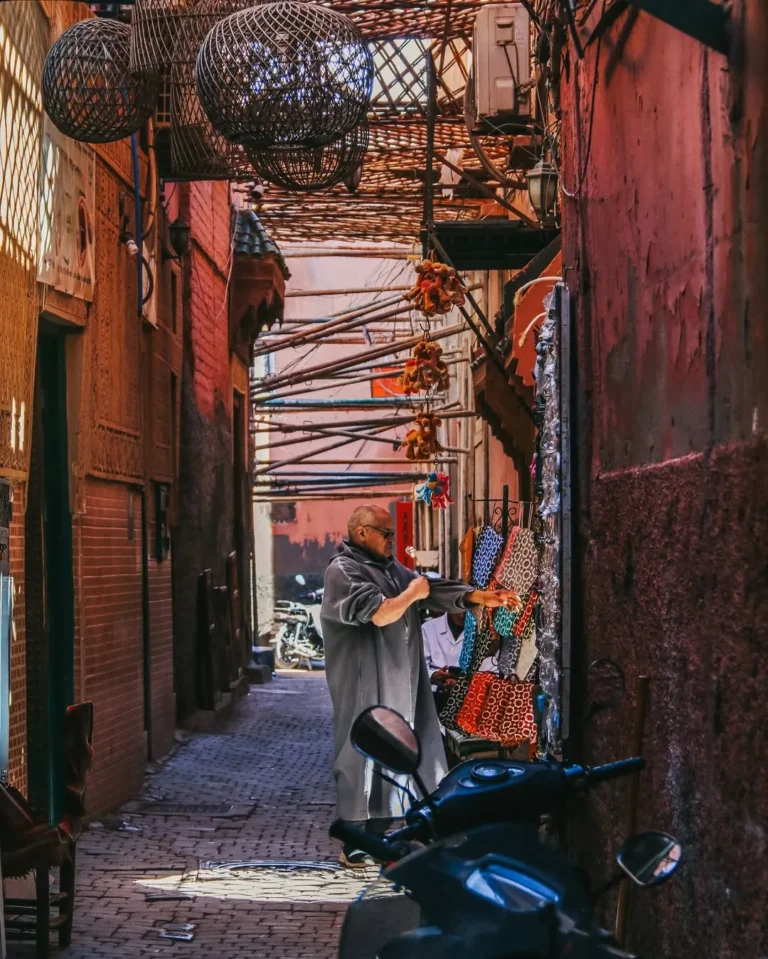 Narrow medina lane hung with lanterns and woven goods