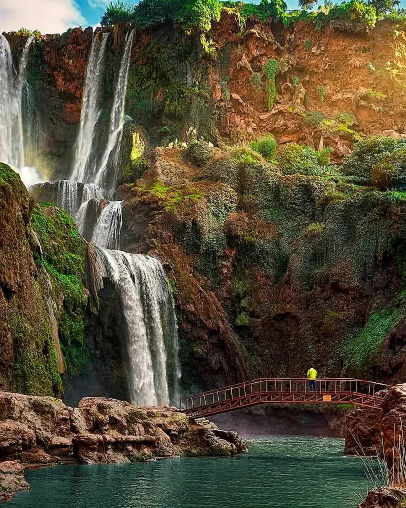 The Ouzoud waterfalls falling into a green pool with a footbridge below