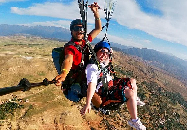 Tandem paragliding pilot and passenger flying over dry hills and plains