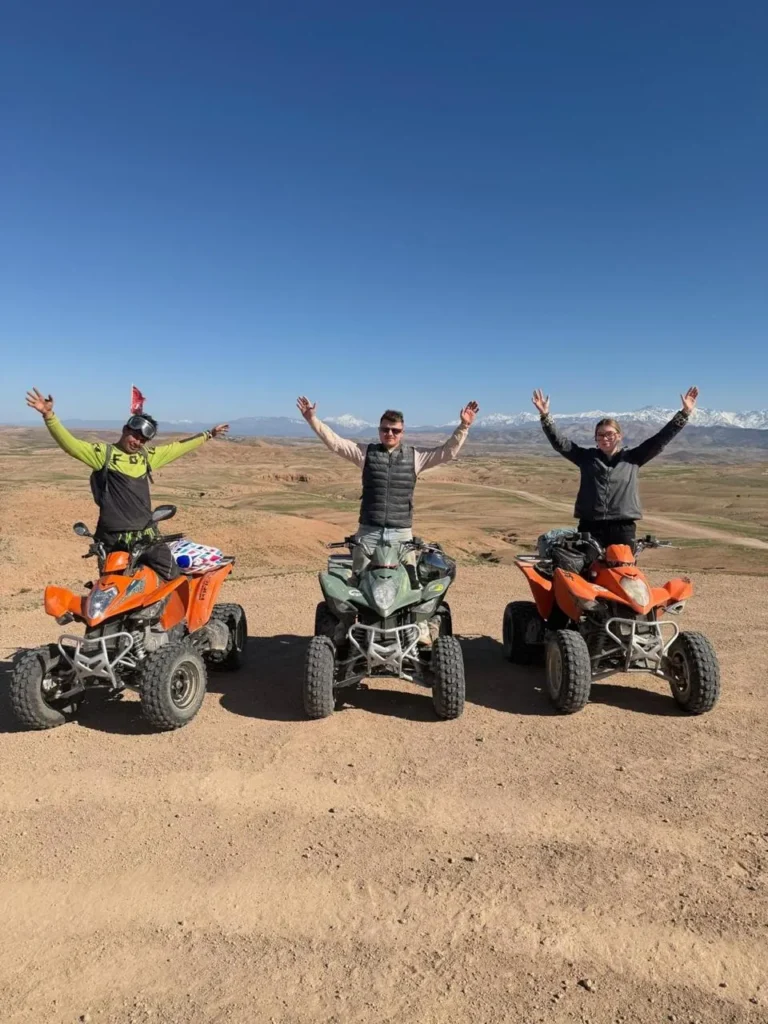 Three riders on quad bikes on the Agafay plateau with the Atlas behind
