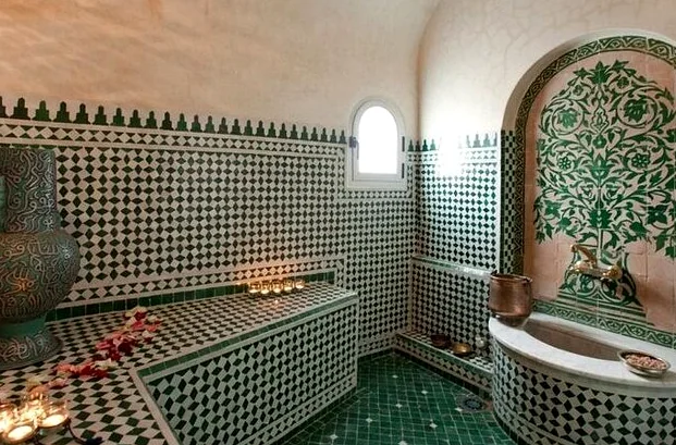 Hammam room with green and white zellige tiles, candles and a marble basin